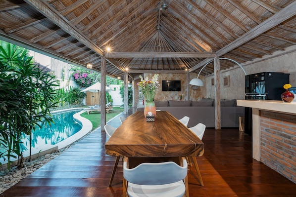 Relax in a spacious living area with a dining table, pool, and lush greenery.