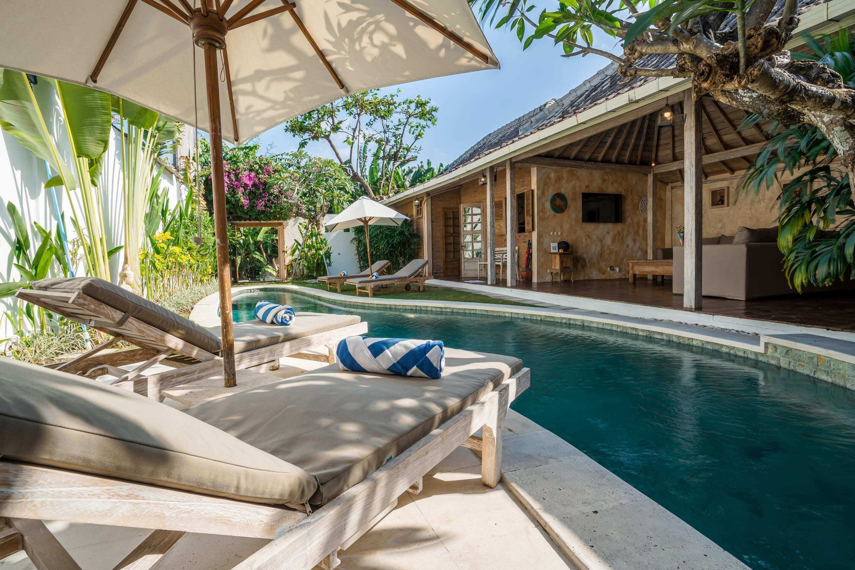 A poolside area with lounge chairs and umbrellas, surrounded by lush tropical plants.