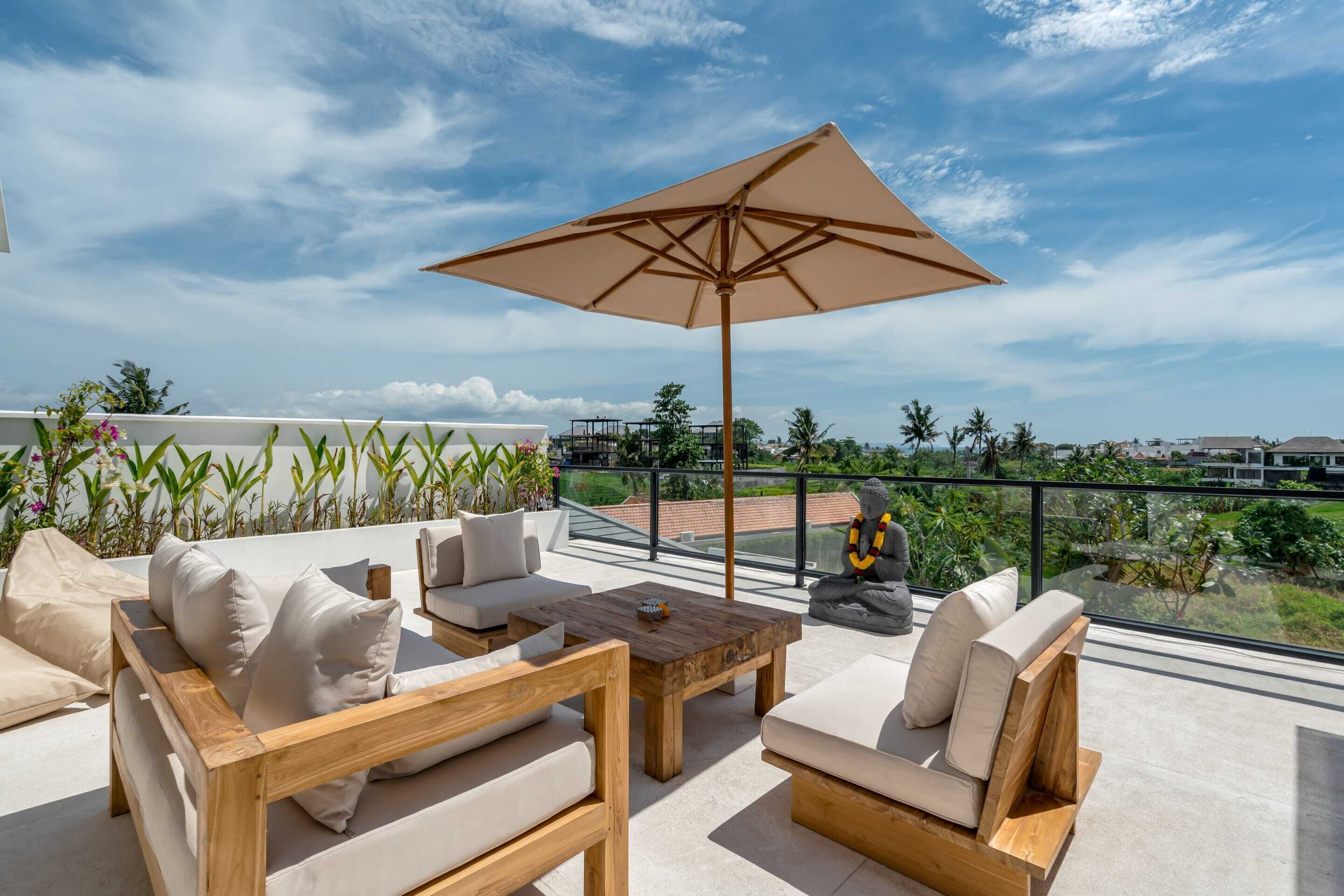 A rooftop terrace with wooden furniture, a large umbrella, and a view of the cityscape.