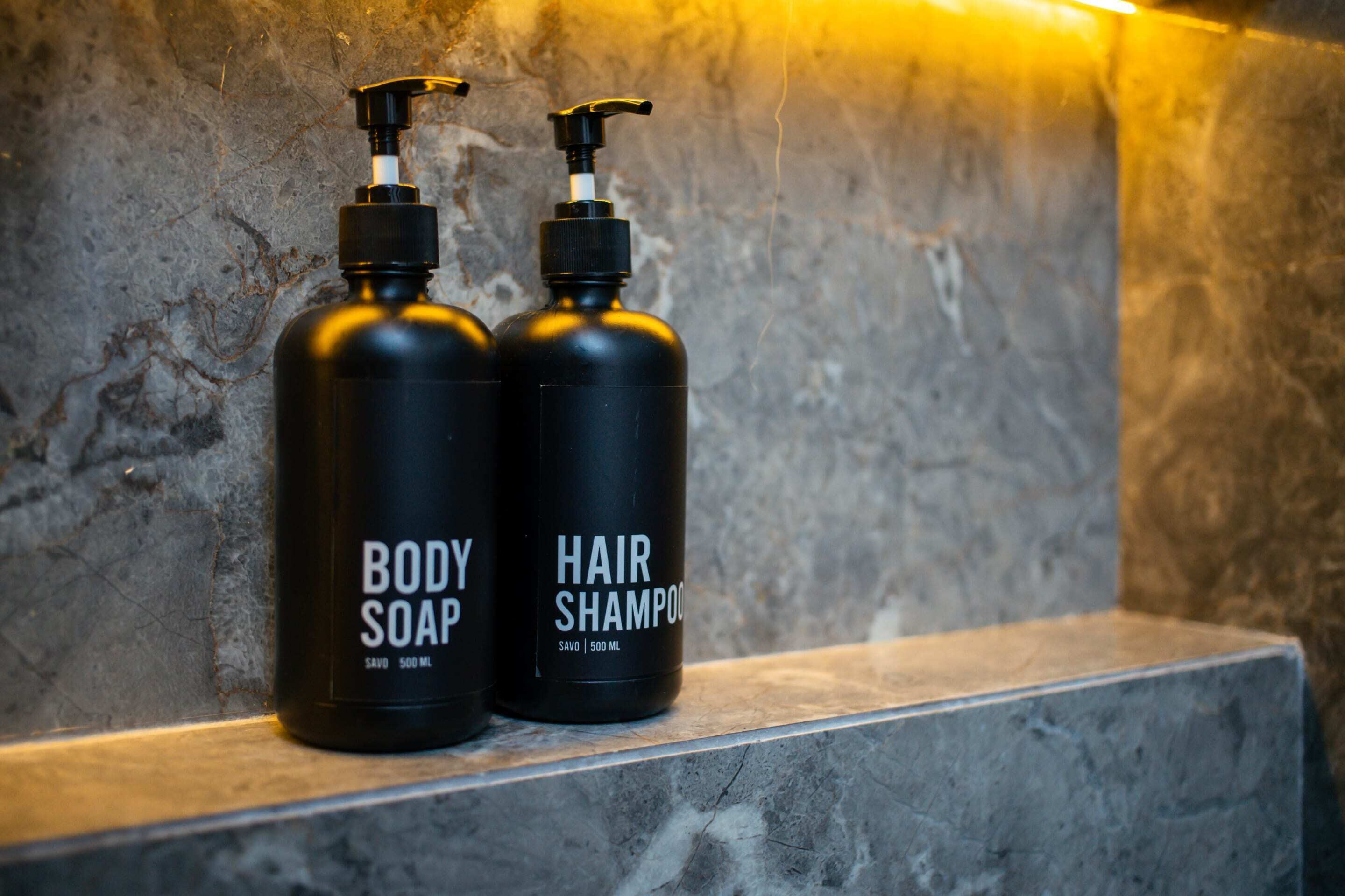Two black bottles of body soap and hair shampoo on a marble ledge.