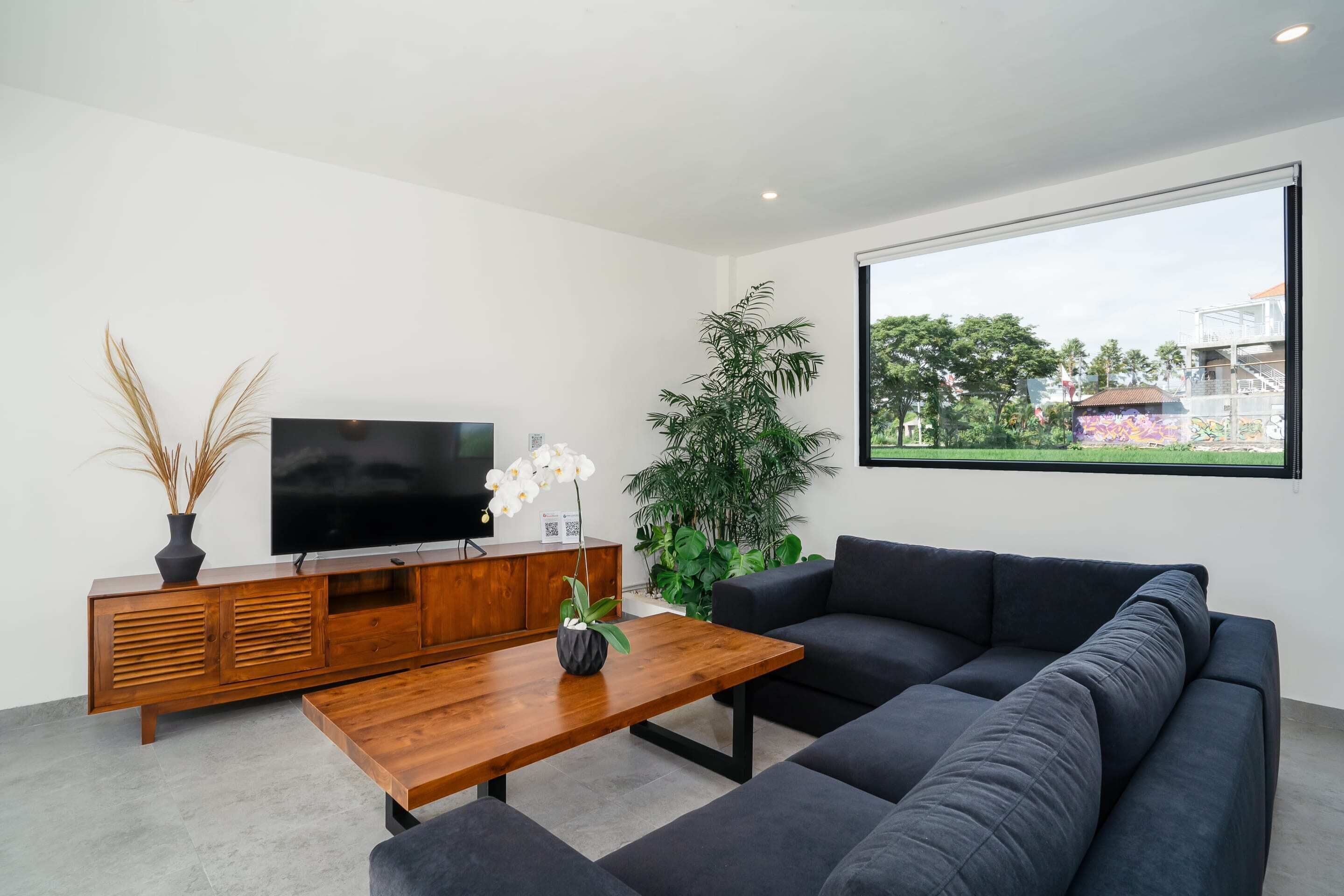 Un salon moderne avec un grand téléviseur à écran plat, un canapé foncé, une table basse en bois et une plante en pot.