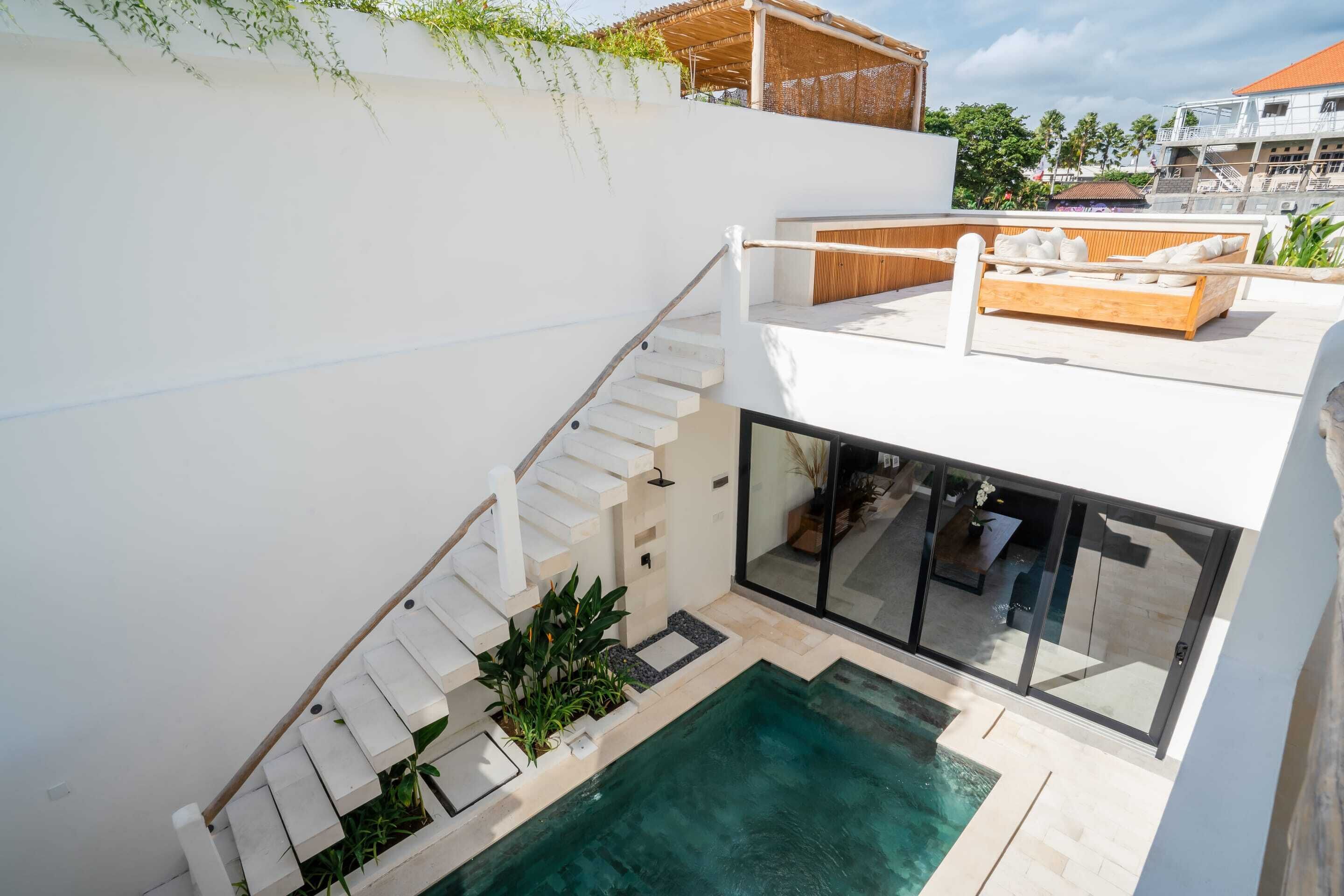 A modern outdoor pool area with a staircase leading to a deck, surrounded by greenery and a view of the city.