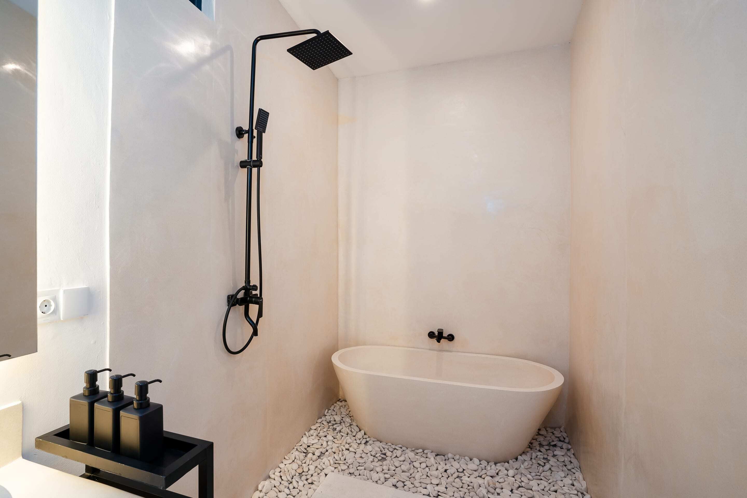 A modern bathroom with a freestanding bathtub, a handheld showerhead, and a small shelf with toiletries.