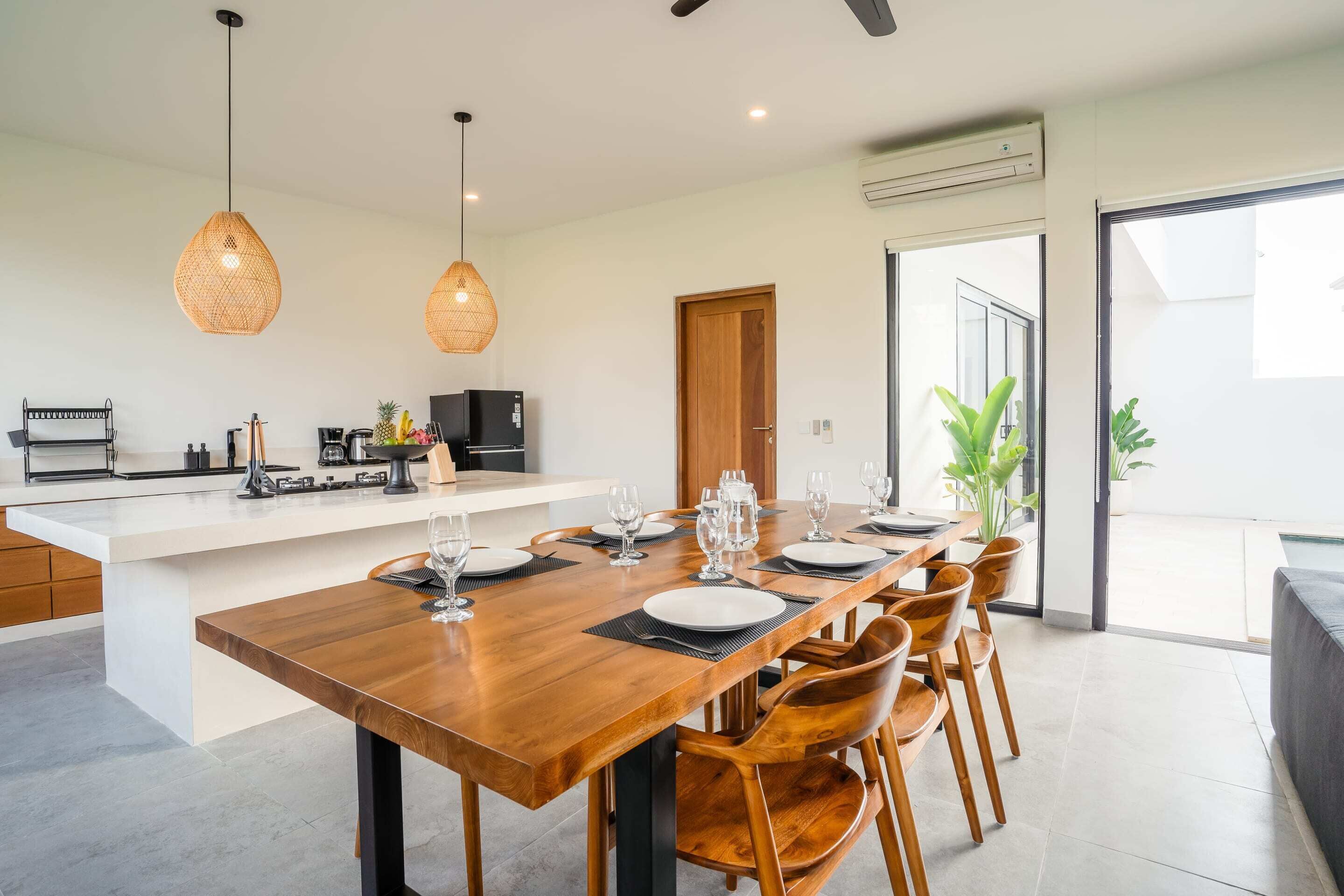 A modern kitchen with a central island, dining table set for six, and a large sliding glass door leading to a balcony.