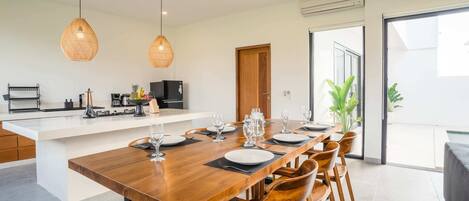 A modern kitchen with a central island, dining table set for six, and a large sliding glass door leading to a balcony.