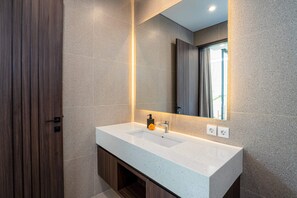 Un baño moderno con encimera blanca, un espejo grande y una puerta de madera.