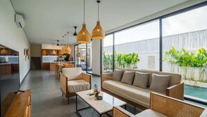 Una sala moderna con sofá, sillones y una mesa de centro. Se observa un ventanal con vistas a una piscina y zonas verdes.