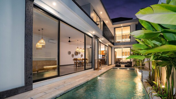 Una casa moderna con piscina, grandes puertas de cristal y un balcón.