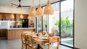 Una cocina moderna con armarios de madera, un comedor con una mesa dispuesta para cuatro personas y vistas a una piscina.
