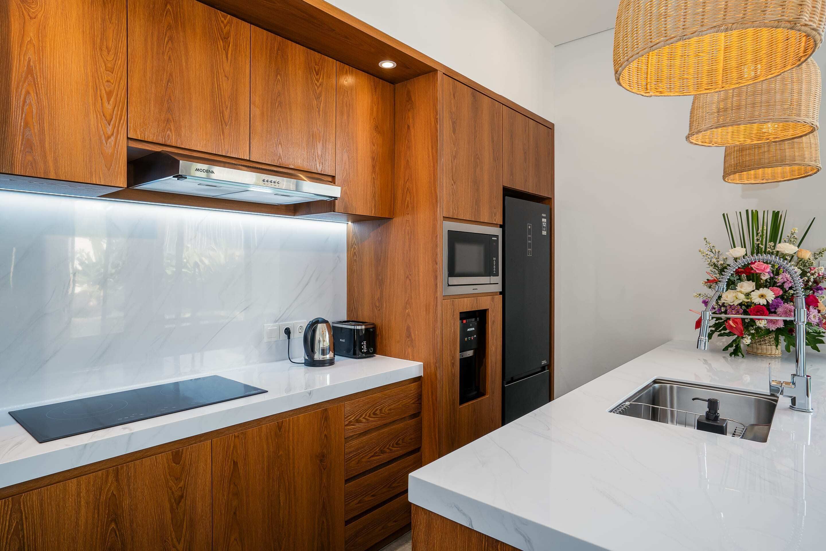 Une cuisine moderne avec des meubles en bois, un four à micro-ondes encastré, un réfrigérateur en acier inoxydable et un plan de travail en marbre blanc.