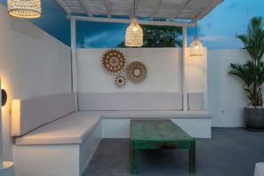 A covered outdoor seating area with a bench and a table, decorative wall art, and pendant lighting. - Villa Quiet (Canggu)