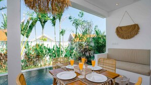A dining area with a pool view, wicker furniture, and a hanging basket. - Villa Zahka (Munggu)