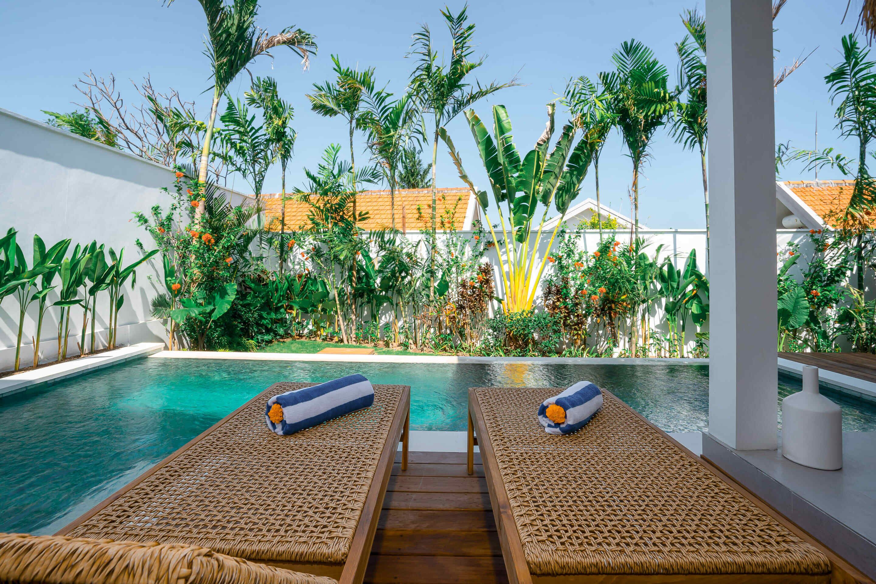 A pool area with two loungers, a wooden deck, and tropical plants.