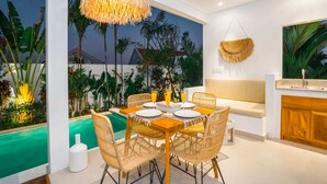 A dining area with a pool view, wicker chairs, a hanging light fixture, and a wooden bench. - Villa Zahka (Munggu)