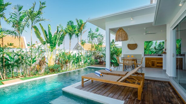 A modern pool area with wooden loungers, a small waterfall feature, and lush tropical vegetation surrounding the space. - Villa Zahka (Munggu)