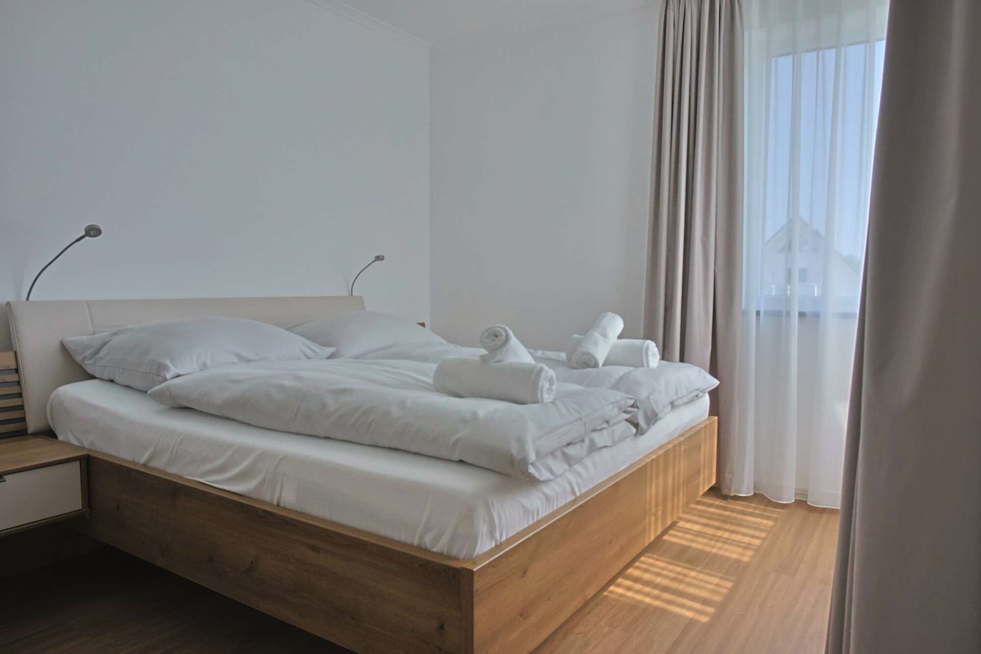 A modern bedroom with a wooden bed, white linens, and neatly folded towels.