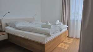 Une chambre à coucher moderne avec un lit en bois, du linge de lit blanc et des serviettes soigneusement pliées.