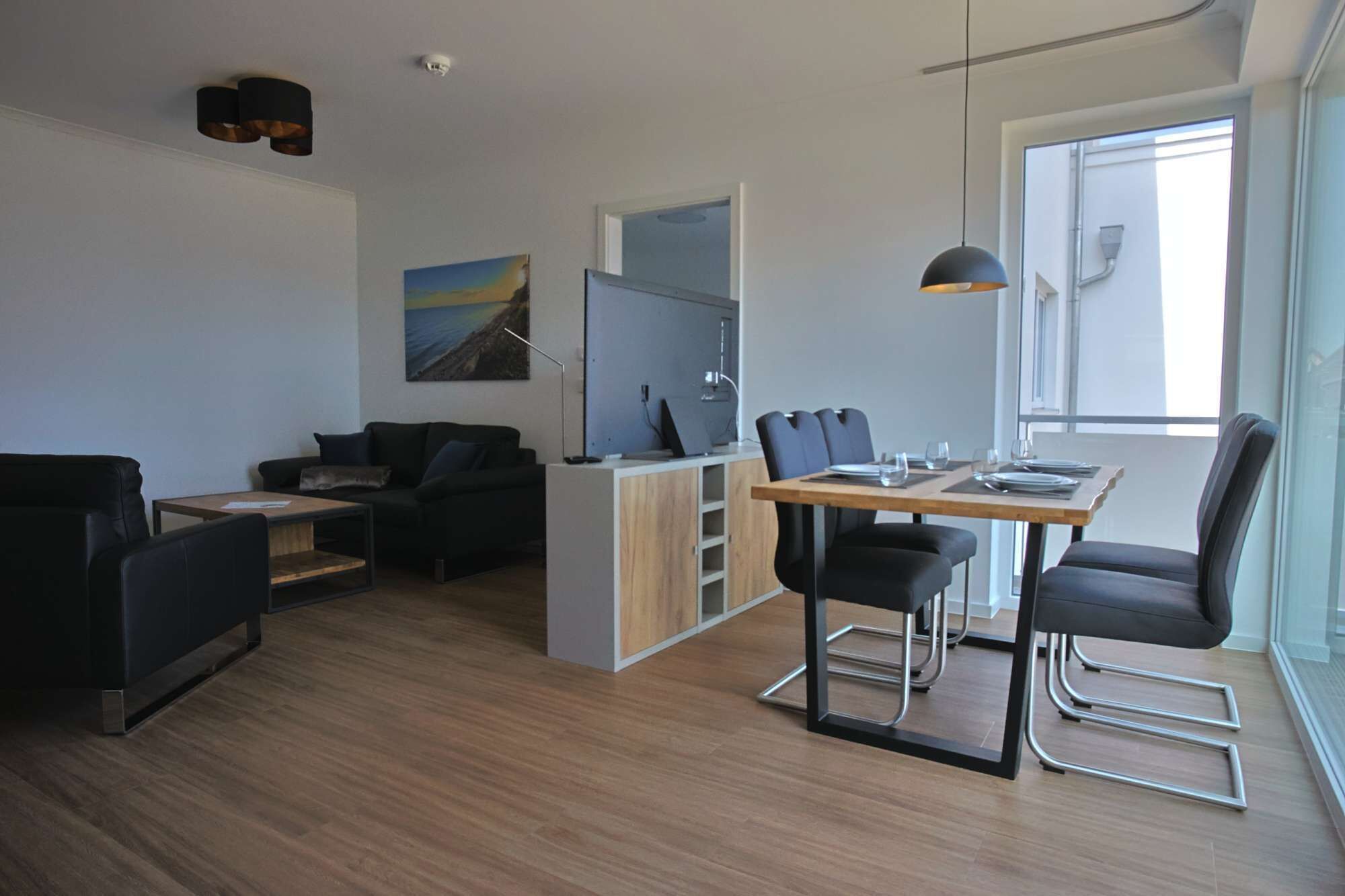 Ein moderner Wohnraum mit Essbereich, einer Couch, einem Fernseher und einem großen Fenster.