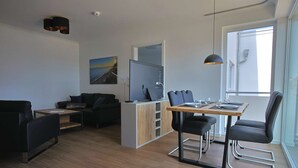 Un espace de vie moderne comprenant un coin repas, un canapé, un téléviseur et une grande fenêtre.