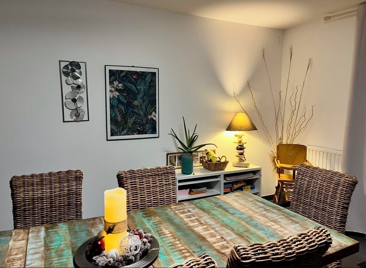 Un comedor con una mesa dispuesta para cuatro personas, rodeada de sillas de mimbre. Una lámpara proporciona iluminación y hay adornos sobre la mesa.