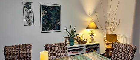 Un comedor con una mesa dispuesta para cuatro personas, rodeada de sillas de mimbre. Una lámpara proporciona iluminación y hay adornos sobre la mesa.