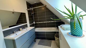 A modern bathroom with a bathtub, two sinks, a shower, and a potted aloe vera plant.