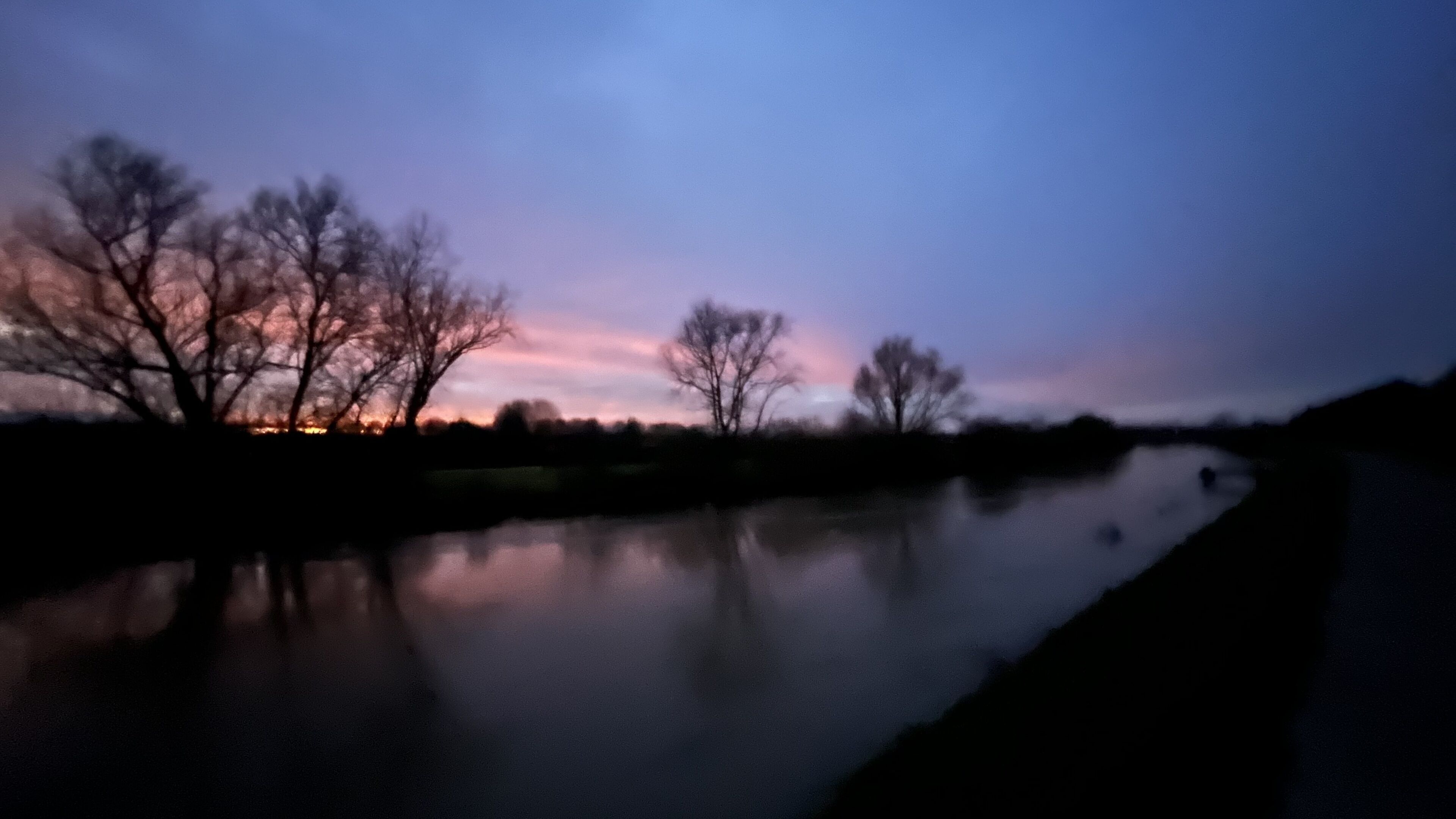 A calm river at dusk with bare trees reflecting the sky.