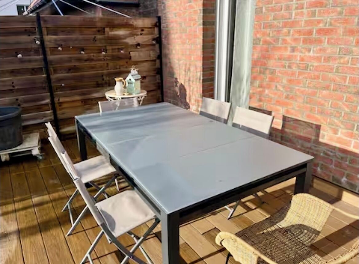 Eine Terrasse mit einem Metalltisch und -stühlen, einer Ziegelwand und einem Holzzaun.