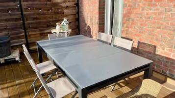 Eine Terrasse mit einem Metalltisch und -stühlen, einer Ziegelwand und einem Holzzaun.