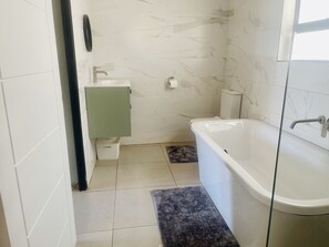 A bathroom with a white bathtub, a green cabinet, and a marble-tiled wall. - Room in B&B - Trendybliss Guest House - N0296 (Thabazimbi)