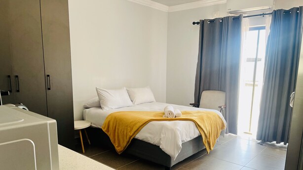 Habitación de hotel moderna con cama, mesita de noche, una silla y zona de baño con bañera e inodoro.