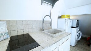 A compact kitchen with a built-in induction cooktop, a sink, and stacked appliances including a washing machine and a microwave. - La Goletta, terrace with a sea view (Portoferraio)