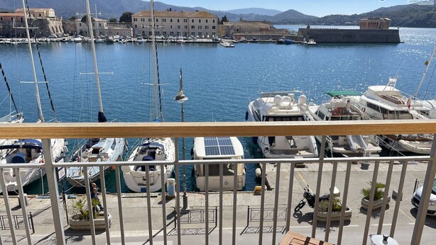 A marina with boats docked, a view of a historic building, and a table with a coffee pot and magazines. - La Goletta, terrace with a sea view (Portoferraio)