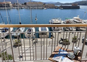 A marina with boats docked, a view of a historic building, and a table with a coffee pot and magazines. - La Goletta, terrace with a sea view (Portoferraio)