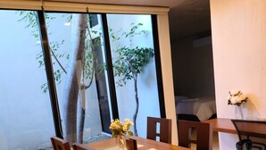 A dining area with a wooden table and chairs, a ceiling fan, and a view of trees through large windows. - Apartment with pool, Wifi, Central, Equipped, shops - Amapola *Mi Amado Chemby* (Mérida)