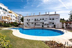 A modern white building with a swimming pool, surrounded by well-maintained lawns and other similar buildings. - Poolside  2 bedroom apartment sunny retreat   REF052 (Benalmádena)