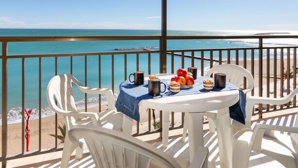 Een balkon met een ontbijttafel, met uitzicht op een strand.