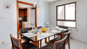 Een moderne eethoek met een glazen tafel, houten stoelen en uitzicht op de keuken en buiten via een groot raam.