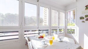 Um quarto claro com janelas amplas, uma mesa posta para o café da manhã e uma varanda com guarda-corpo.