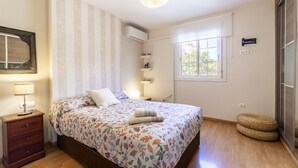 Um quarto com uma cama, mesas de cabeceira, uma luminária, uma janela e um ar-condicionado fixado na parede.