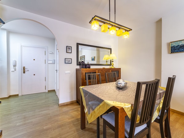A dining area with a wooden table, chairs, a chandelier, a mirror, and a painting on the wall.
