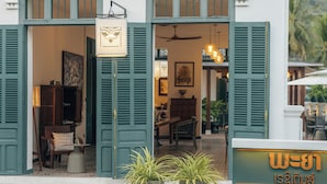 A building with open green shutters, a sign with Thai script, and potted plants on the steps. - Pha Nya Residence (Luang Prabang)