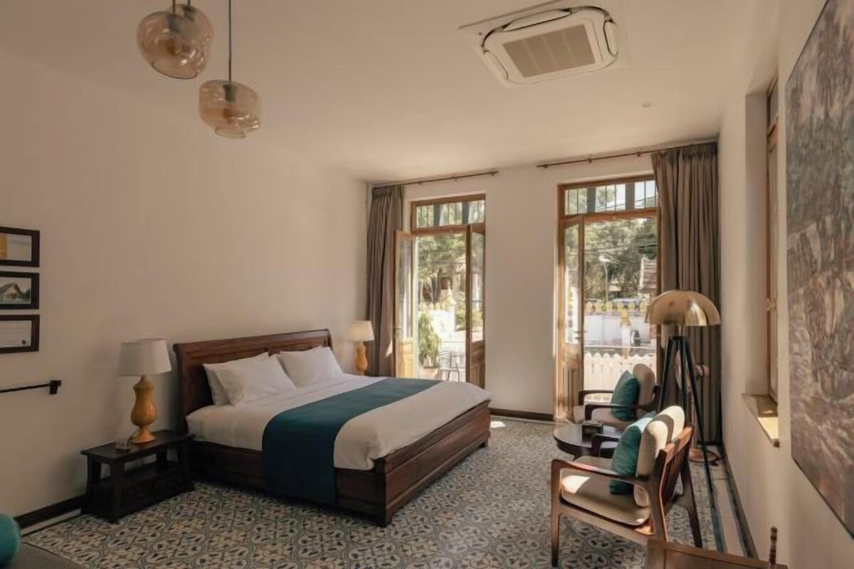 A bedroom with a bed, bedside tables, a chair, a desk, and a large window.