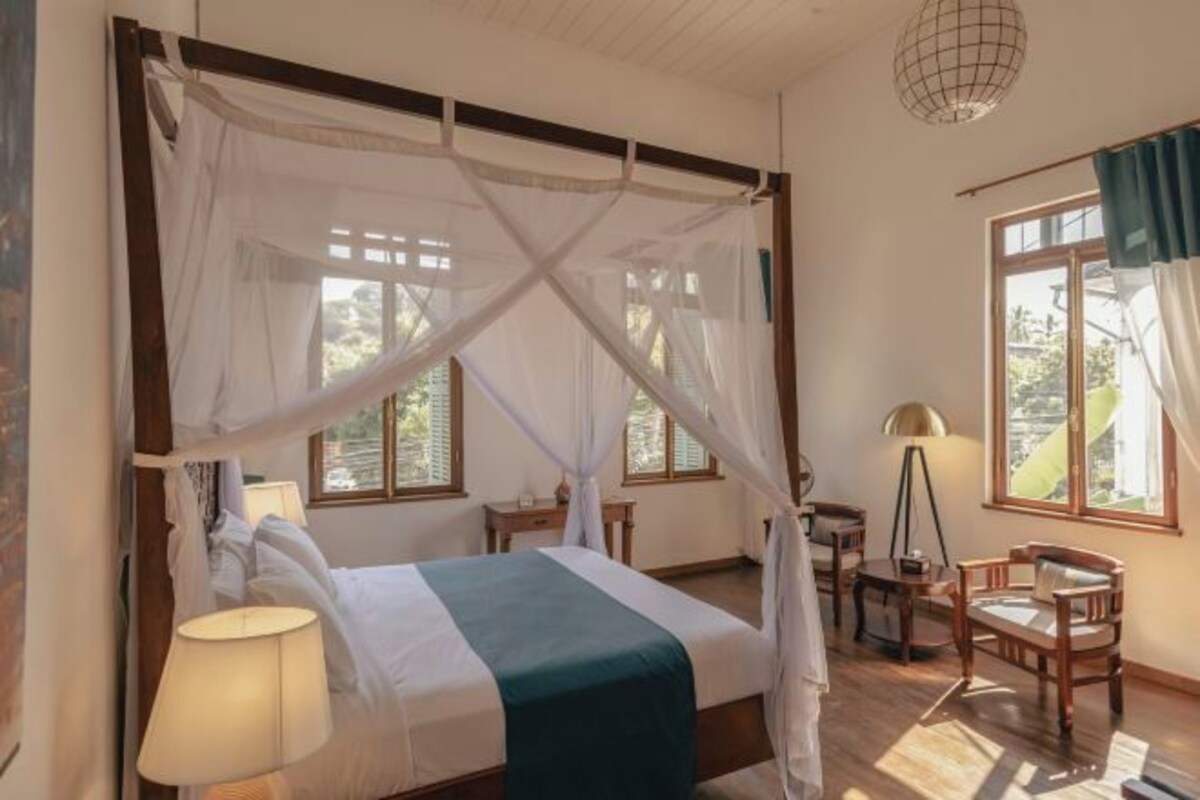 A room with a four-poster bed, a desk, a chair, and a lamp.