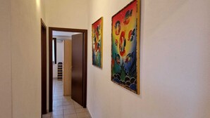 A hallway with a tiled floor, a wooden door, and two colorful paintings on the wall. - Maison Maria, 7 beds (Villasimius)