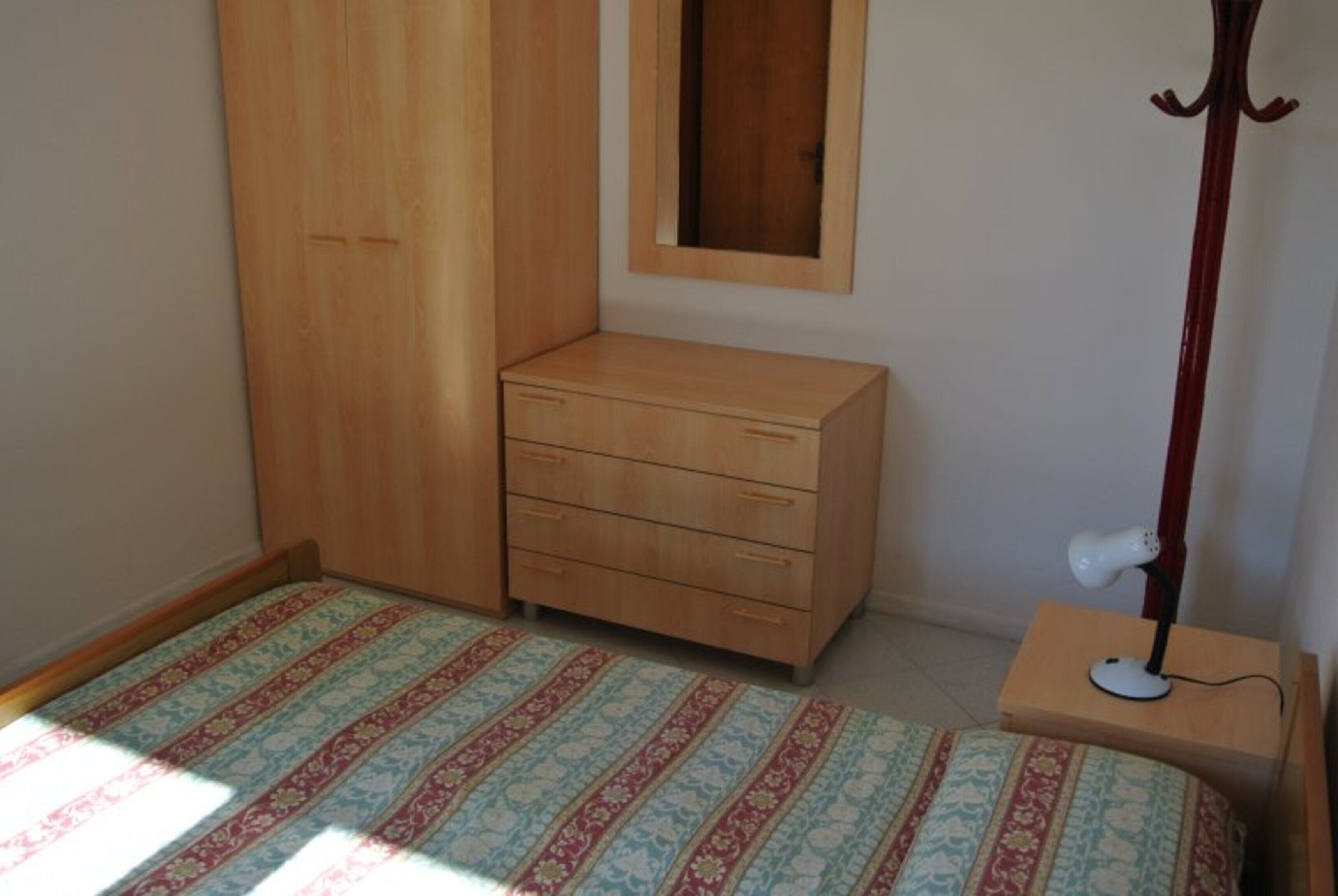 Un dormitorio con una cama, un aparador de madera, un espejo y una lámpara de pie.