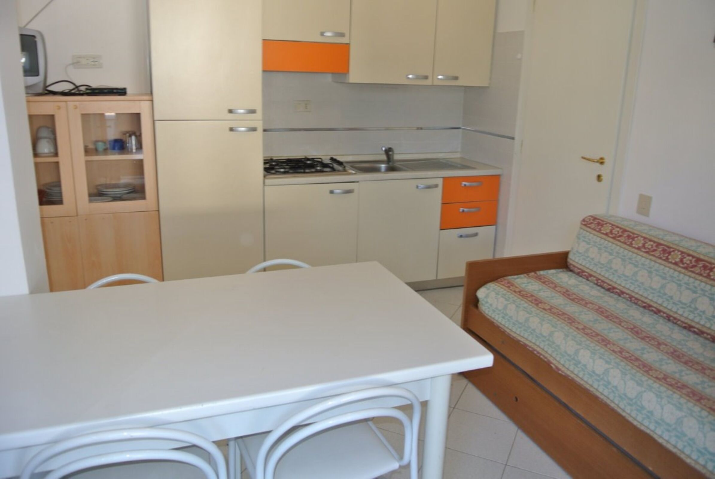 A compact kitchen with a dining table and chairs, a sofa, and a small cabinet with dishes.