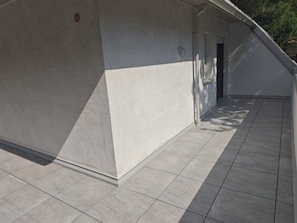 A covered outdoor area with a tiled floor and a white wall.