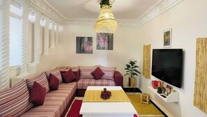 A living room with a sofa, a coffee table, a TV, and a decorative hanging light fixture. - Coquet Appartement À Casablanca (Casablanca)