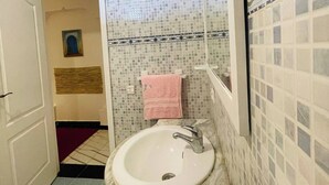 A bathroom with a white sink, a mirror, and a tiled wall. - Coquet Appartement À Casablanca (Casablanca)